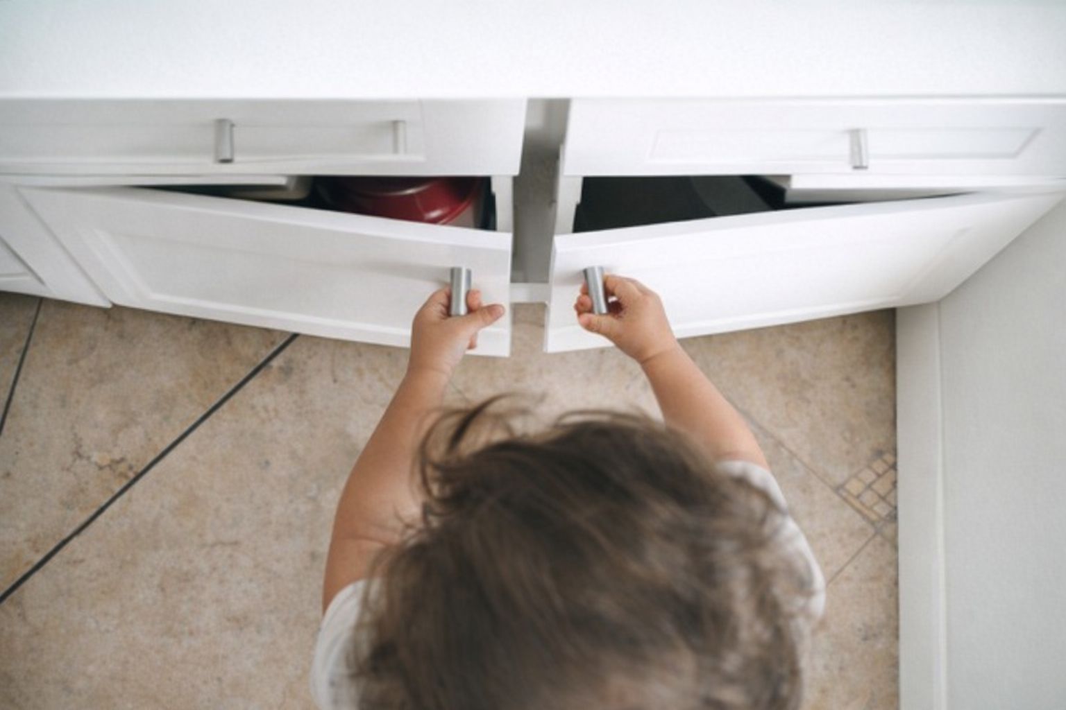 Pieni lapsi avaamassa valkoisia keittiön kaappeja vetimistä kiinni pitäen.
